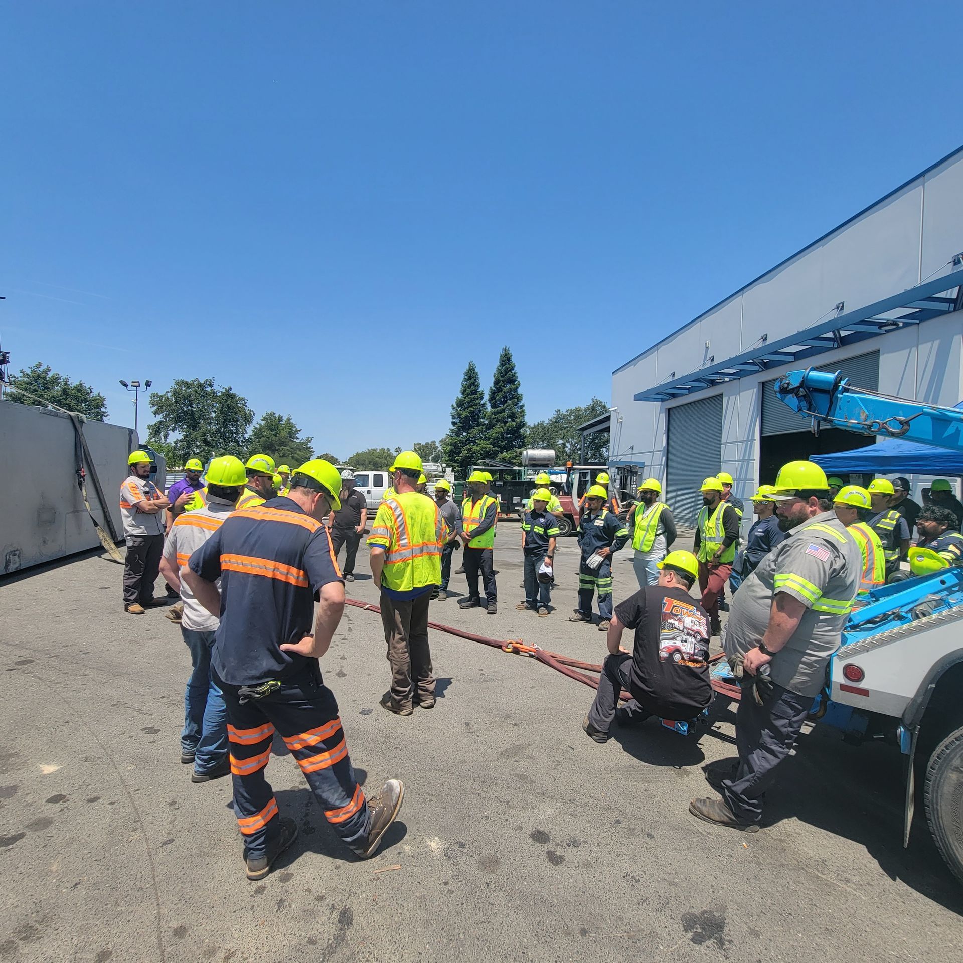 Utility workers in high-visibility gear gathered beside a white truck at an outdoor industrial site.