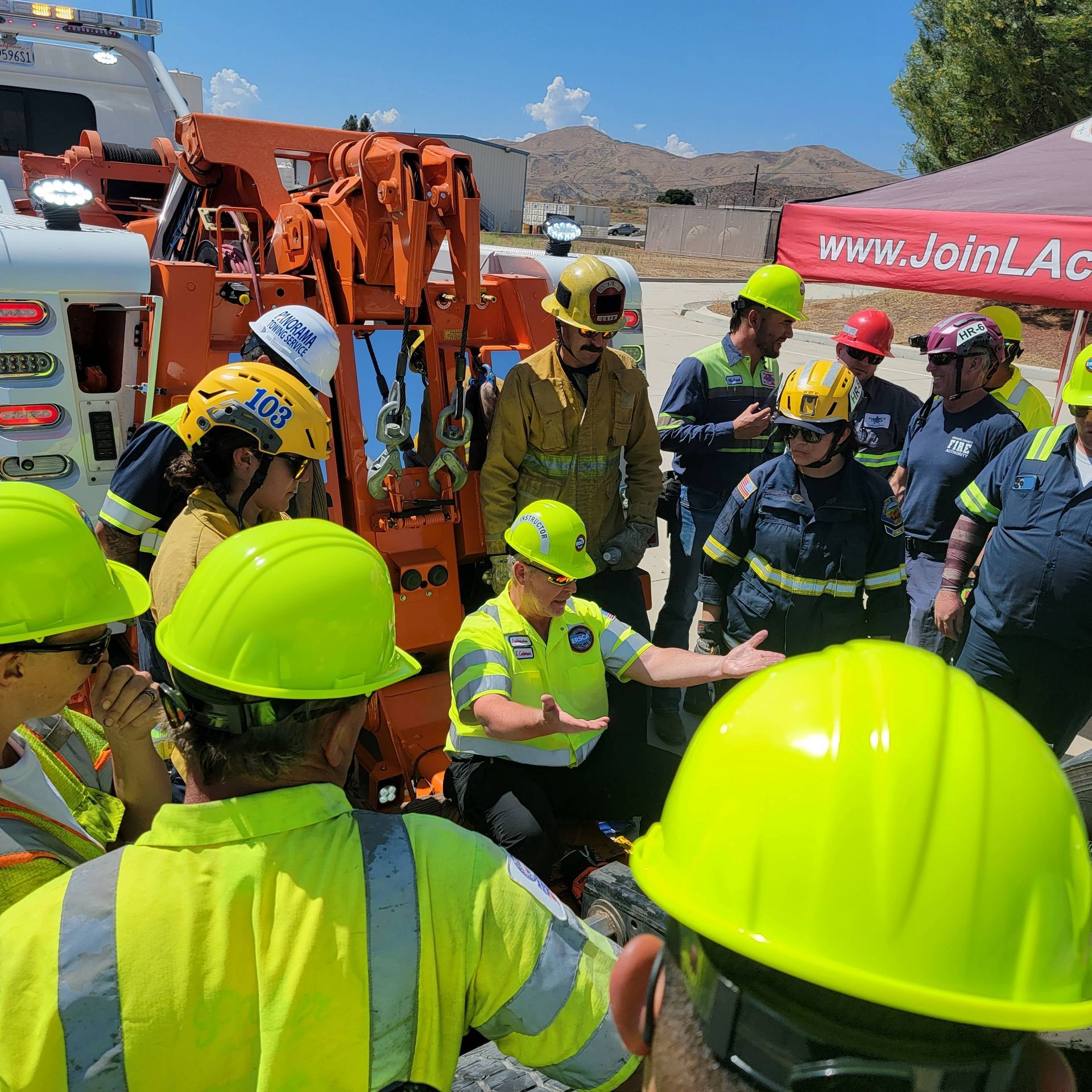 Workers in hard hats gather around an emergency scene beside a fire truck and excavator outdoors.