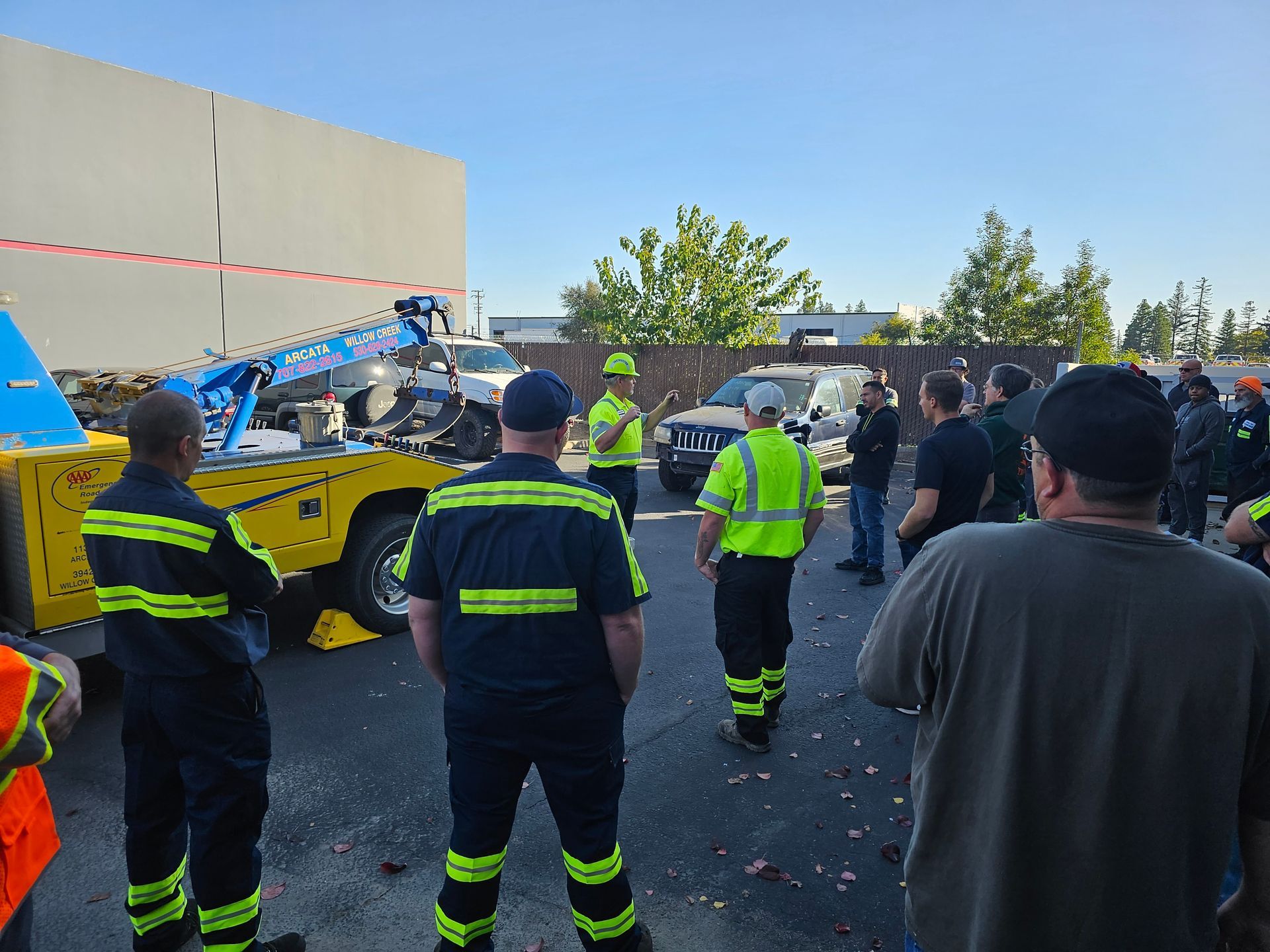Emergency responders and bystanders gather around a yellow tow truck at a roadside scene.