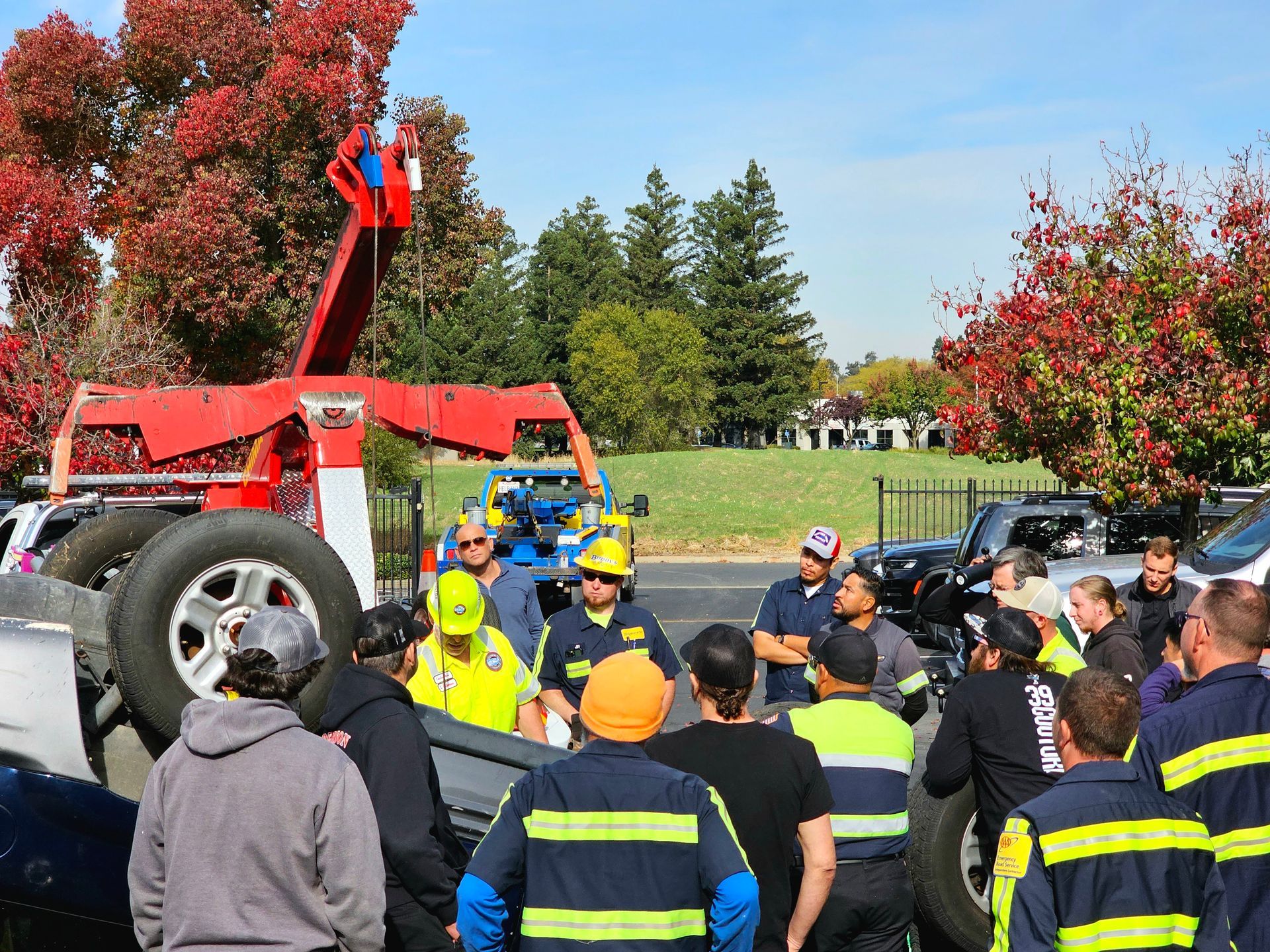Rescue crew in helmets gathers around an overturned car beside a red tow truck on a roadside.