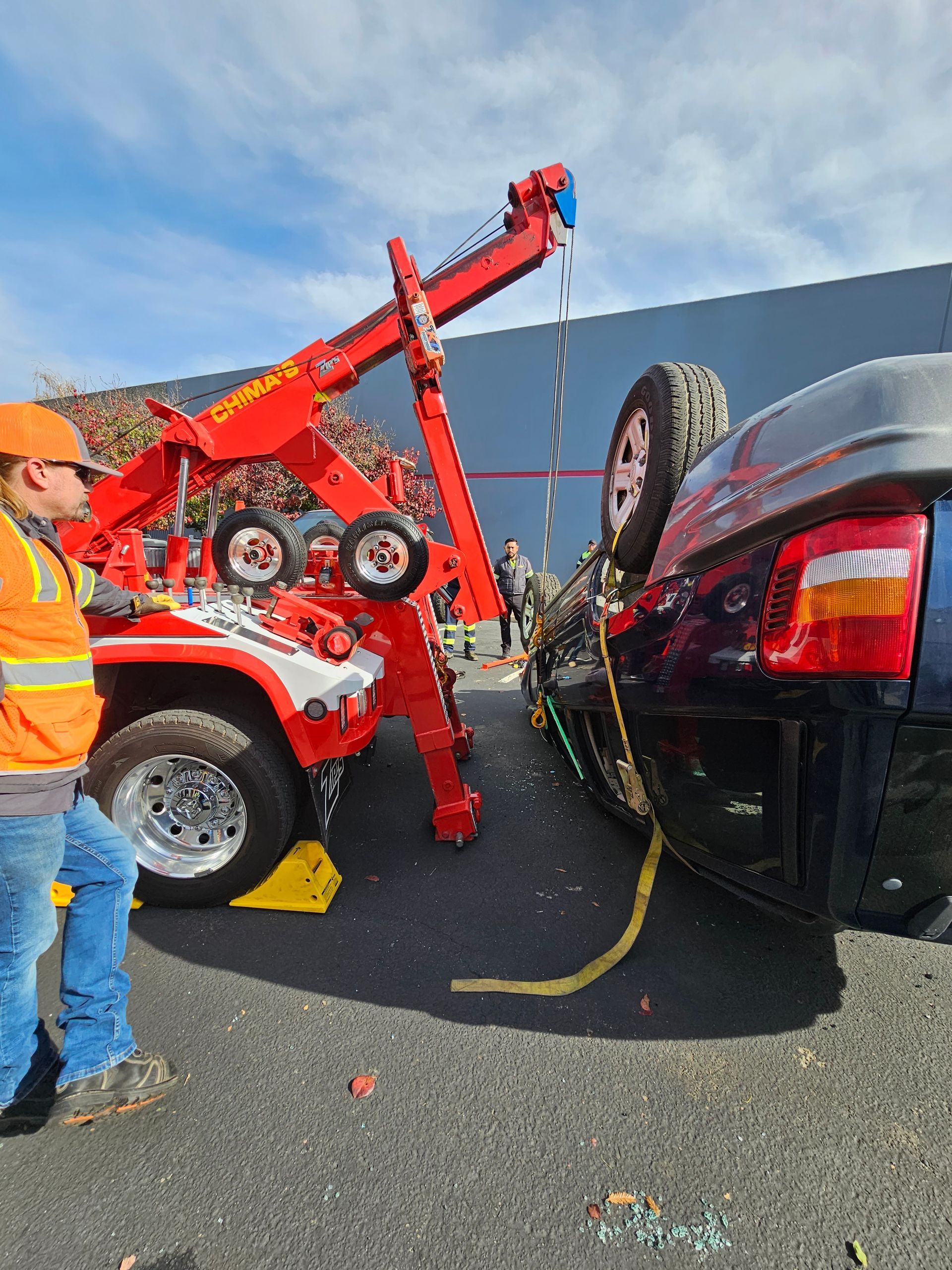 Tow truck lifting a red car beside a black SUV on a road, with a worker in an orange safety vest nearby