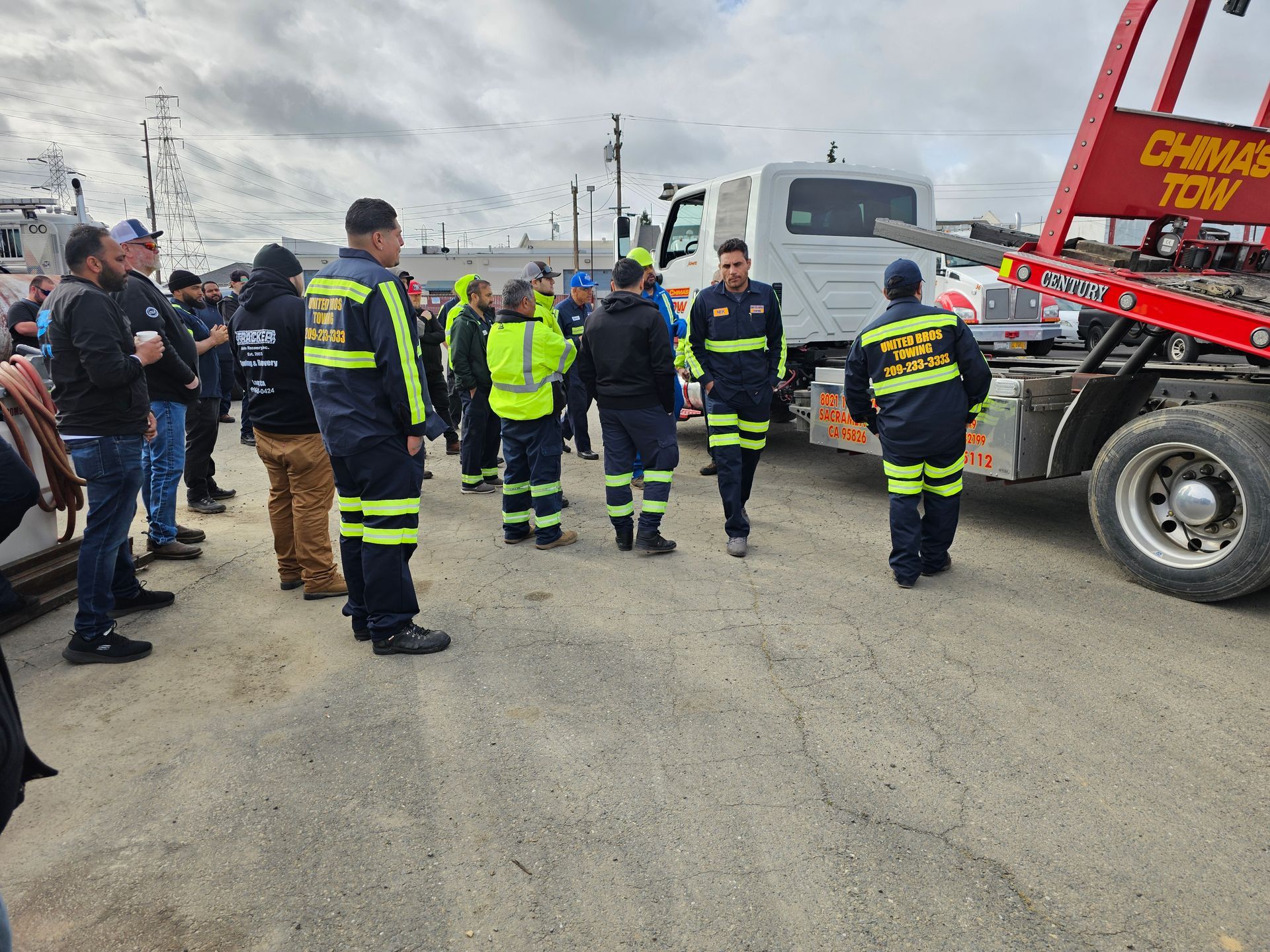 Emergency responders in neon safety gear gather on a road beside a tow truck under cloudy skies