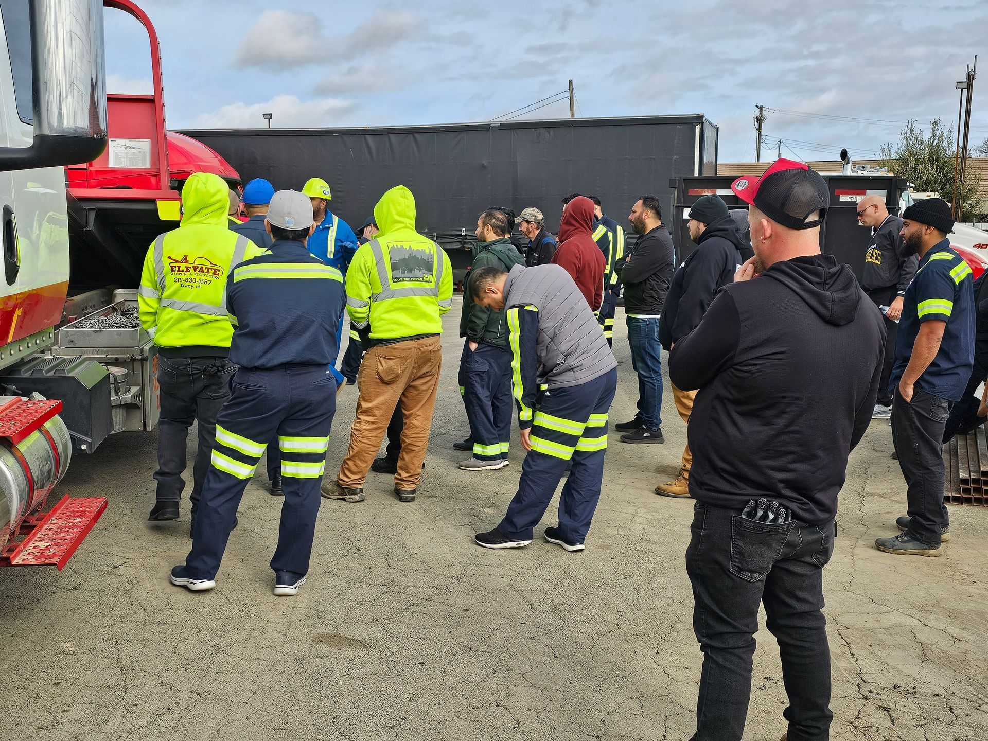 Group of workers in high-visibility gear gathered near a red truck on a gravel site