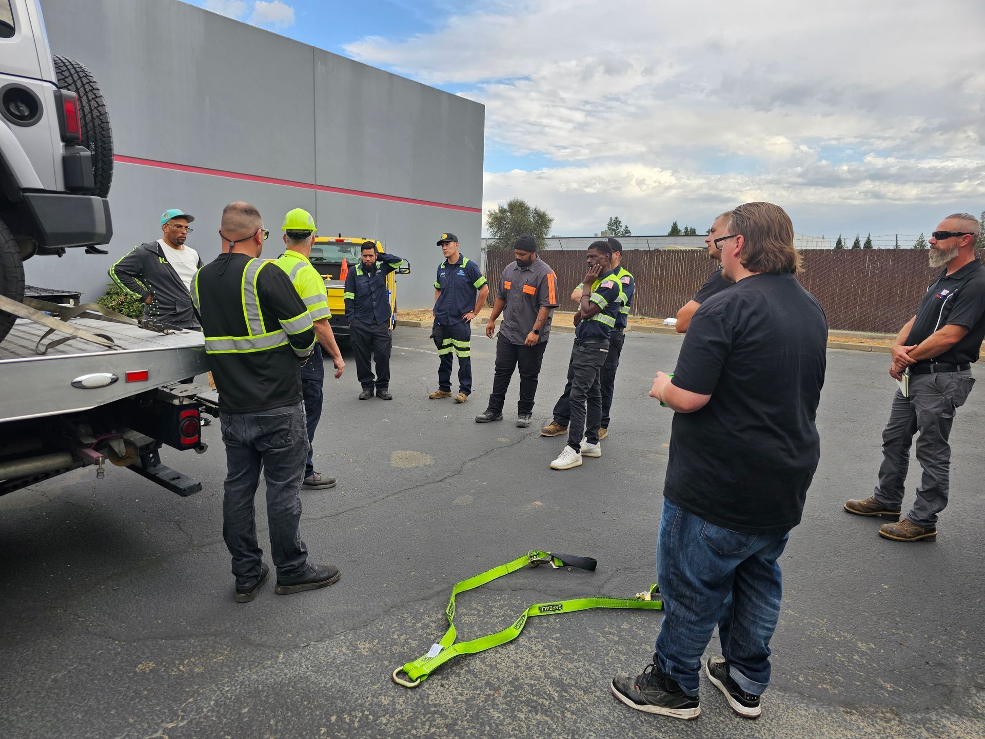 Workers in safety vests gather around a truck in a parking lot during a roadside training session.