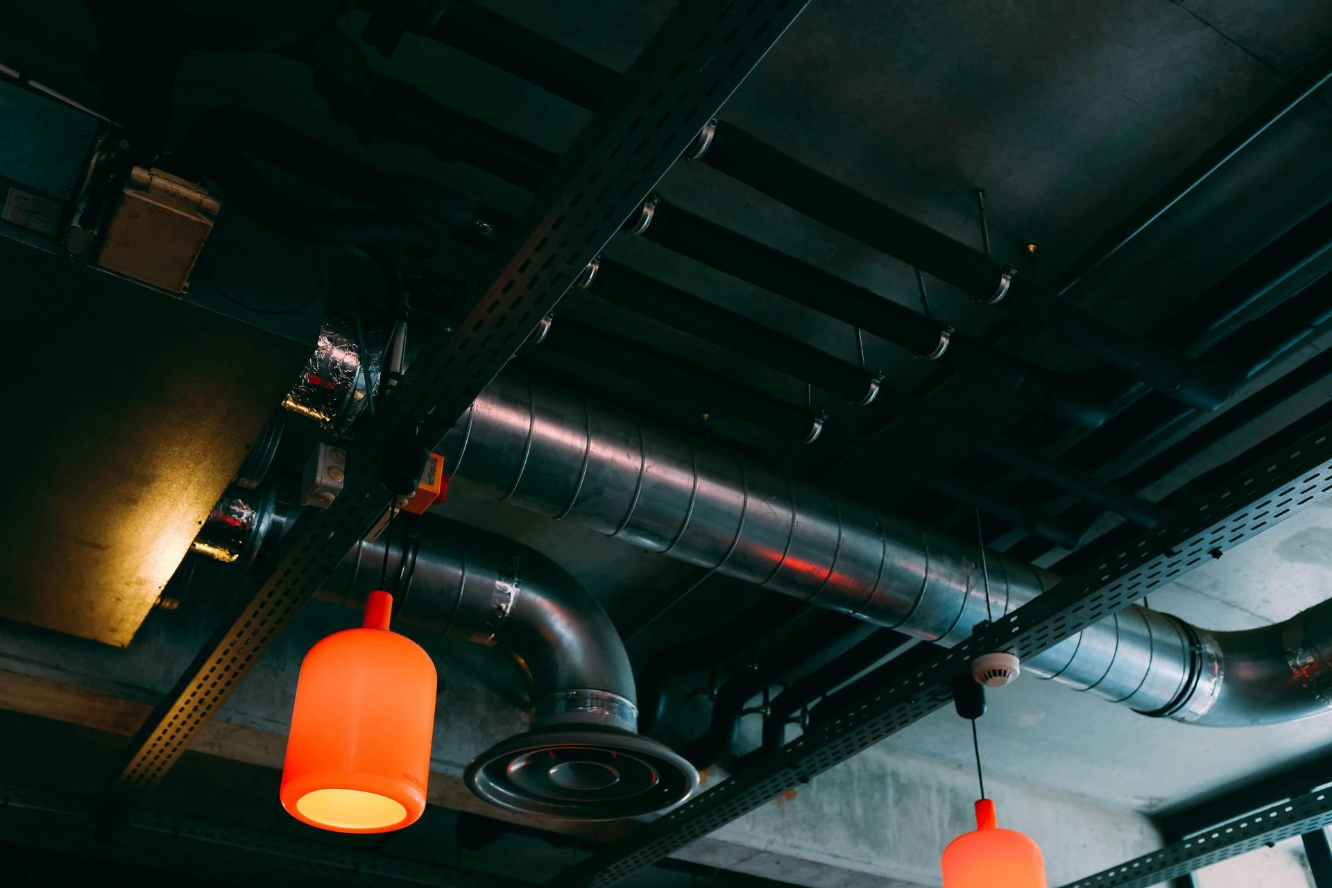 Industrial ceiling with metal pipes, beams, and orange pendant lights.