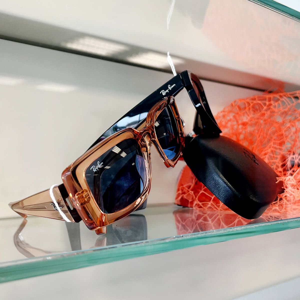 Un paio di occhiali da sole Ray-Ban appoggiati su uno scaffale di vetro