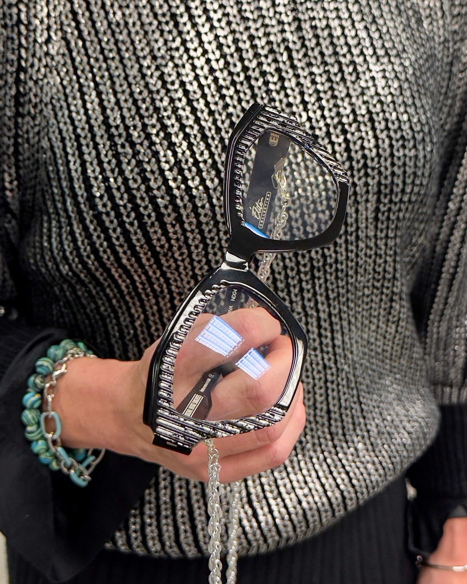 Una donna che indossa un maglione argentato tiene in mano un paio di occhiali da sole
