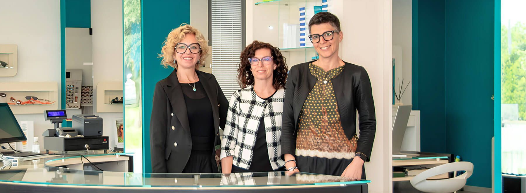 Team di Ottica Elena Battistutta dietro bancone del negozio di ottica.