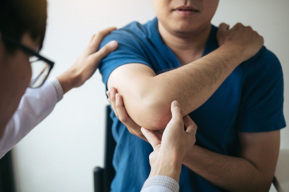A Man is Getting His Elbow Examined by a Doctor — Mark O'Brien Chiropractic in West End, QLD