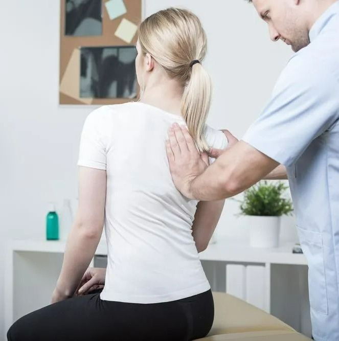 A Woman is Sitting on a Table While a Man Examines Her Back — Mark O'Brien Chiropractic in West End, QLD