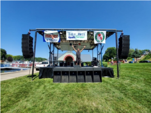 A man stands on a stage sorrounded by ISP Line Array Speakers
