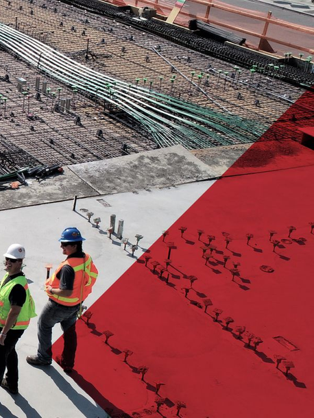 Construction workers in hard hats stand by a concrete slab with rebar at a building site.