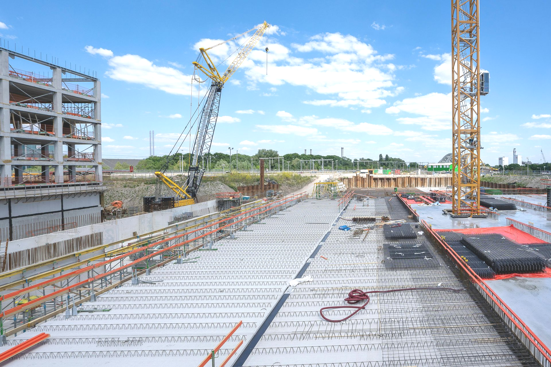 Construction site with concrete slab, crane, and partially built steel structure under a blue sky