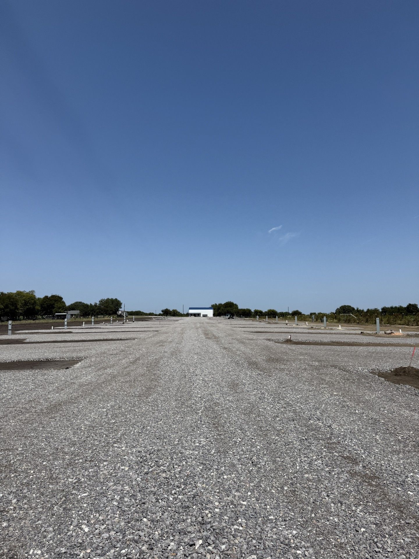 Gravel parking area under a clear blue sky, with a white building in the distance.