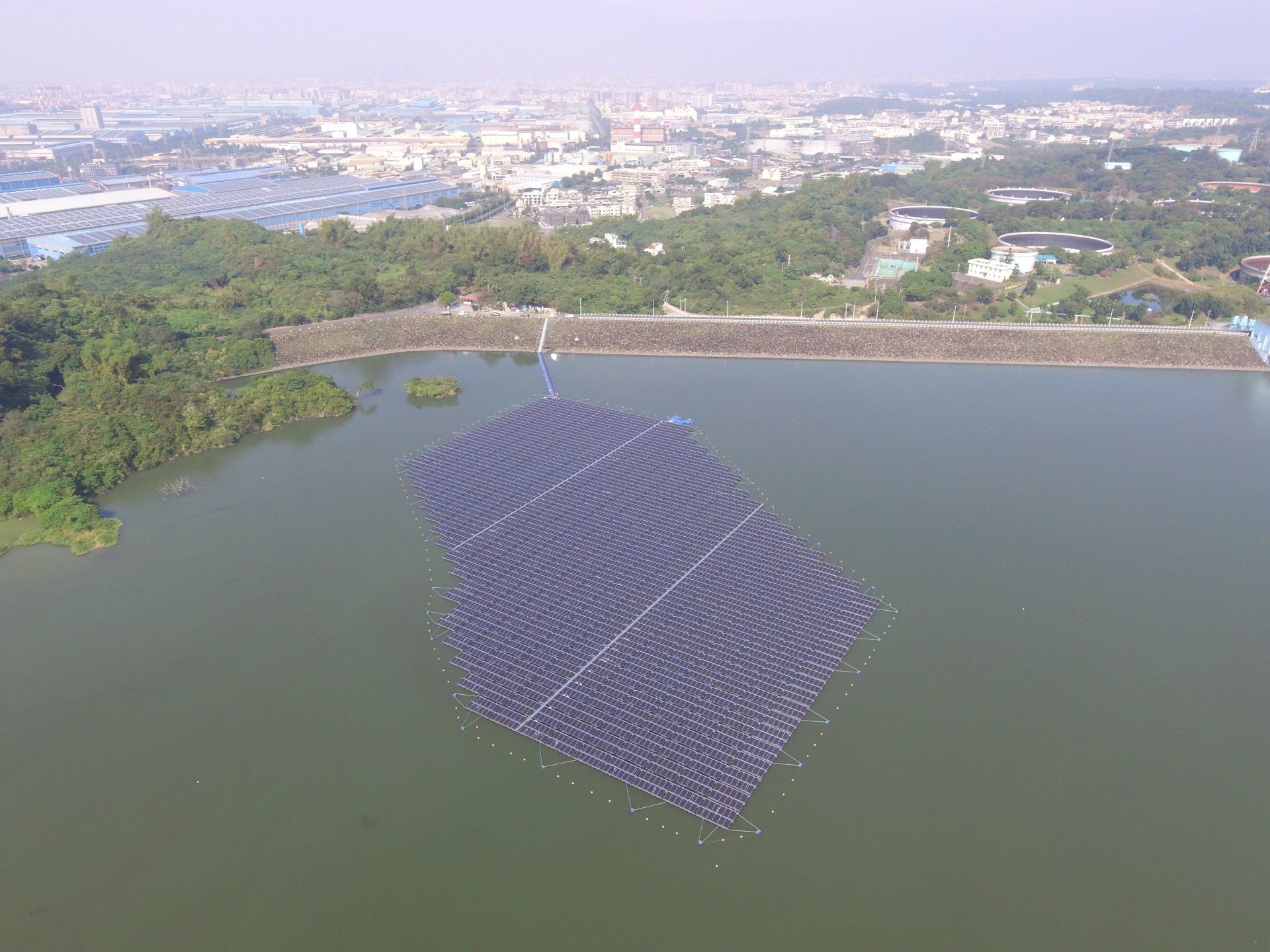 從空中俯瞰湖面上漂浮的大型太陽能電池板陣列，背景是城市景觀。