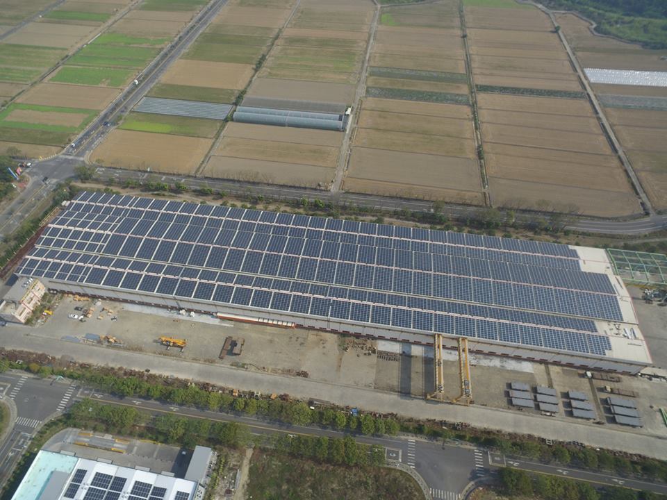 從空中俯瞰，一座大型建築物外牆覆蓋著太陽能電池板，周圍環繞著田野和道路。