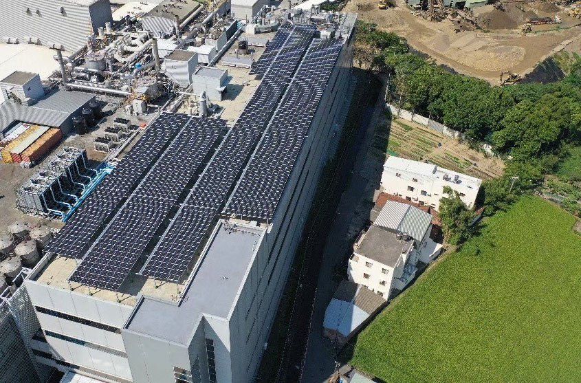 從高處俯瞰一座大型建築物,其屋頂上排列著成排的太陽能電池板,周圍環繞著其他建築物和綠植。