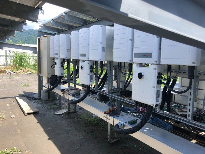 太陽能逆變器安裝在室外金屬支架上，位於太陽能板陣列下方。白色盒子內有電纜。