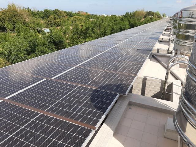 建築物屋頂上的太陽能電池板正在吸收陽光。背景是綠樹和藍天。