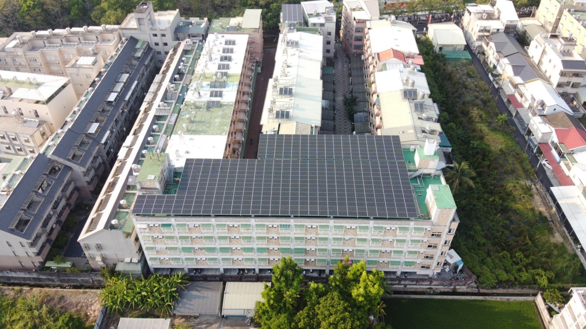 從空中俯瞰，一座屋頂裝有太陽能電池板的建築物，周圍環繞著其他建築物和綠植。