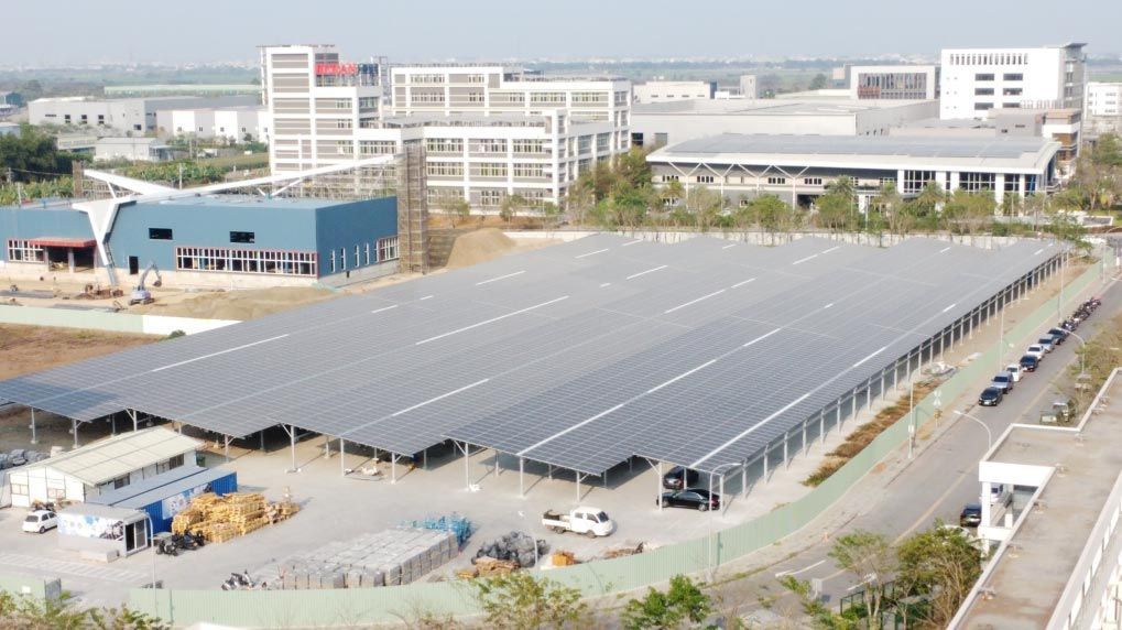 停車場上方架設大型太陽能板陣列，背景是建築物。陽光明媚的戶外環境。