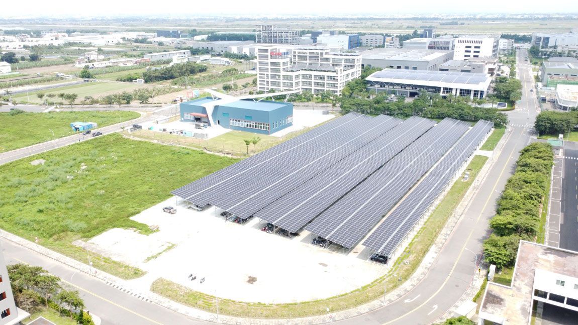 從空中俯瞰，可以看到排列在混凝土空地上的太陽能電池板，旁邊是一片草地和幾棟建築物。