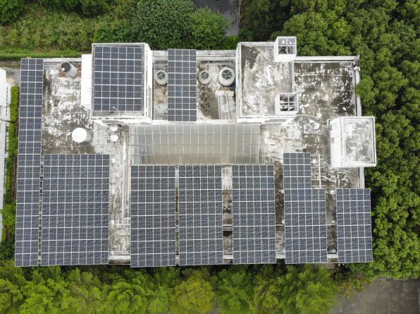 從空中俯瞰，一棟建築物的屋頂覆蓋著太陽能電池板，周圍綠樹環繞。