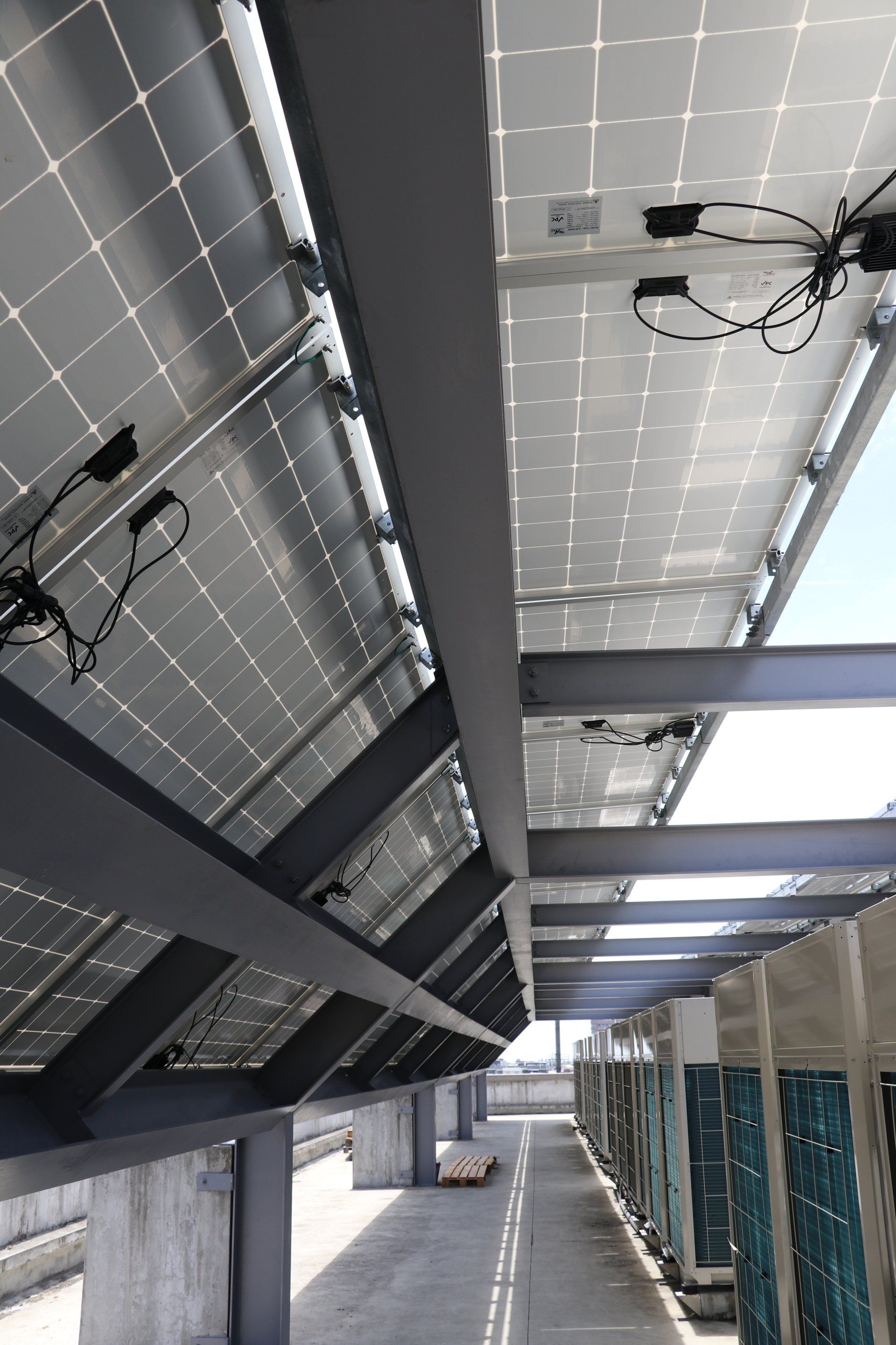 安裝在屋頂一排空調機組上方的金屬框架上的太陽能電池板的底部視圖。