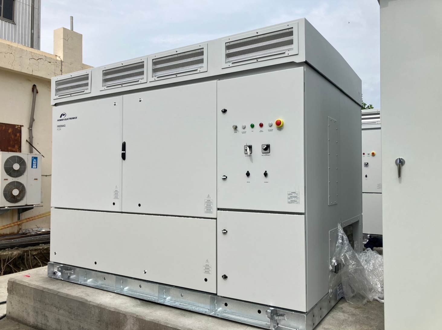 戶外混凝土基座上放置著一個大型矩形淺色電氣設備。通風格柵和控制面板清晰可見。