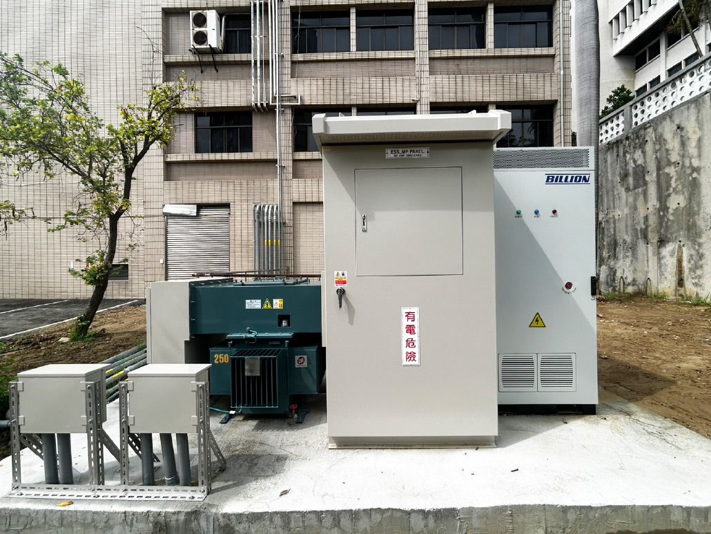 建築物前的室外電氣設備：灰色和藍色的櫃體、混凝土底座、小樹，以及背景中的建築物。