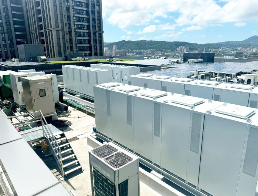 屋頂上排列著一排排白色工業設備，可能是用於發電或冷卻的，附近有城市景觀和山脈。