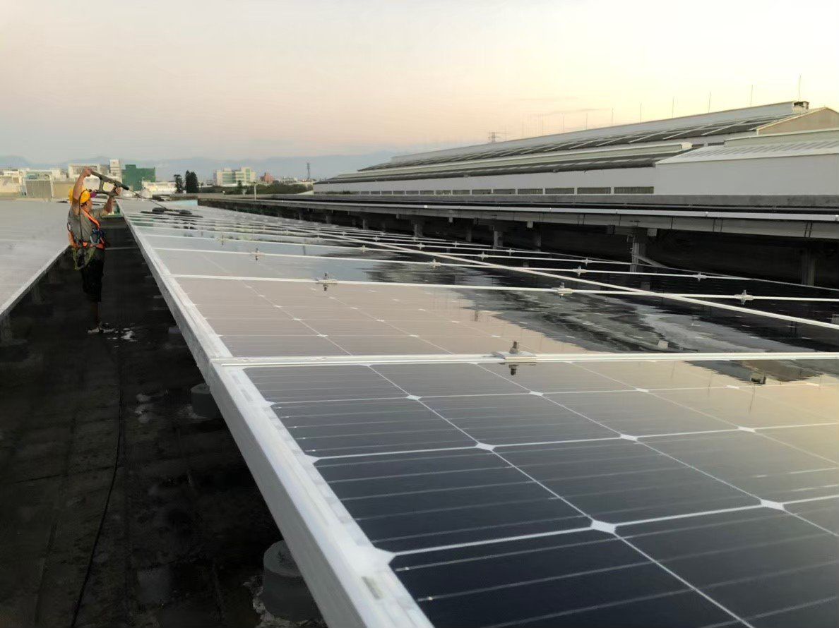 屋頂上的太陽能板反射著天空，背景可以看到工人在工作。這些電池板安裝在平坦的屋頂上。