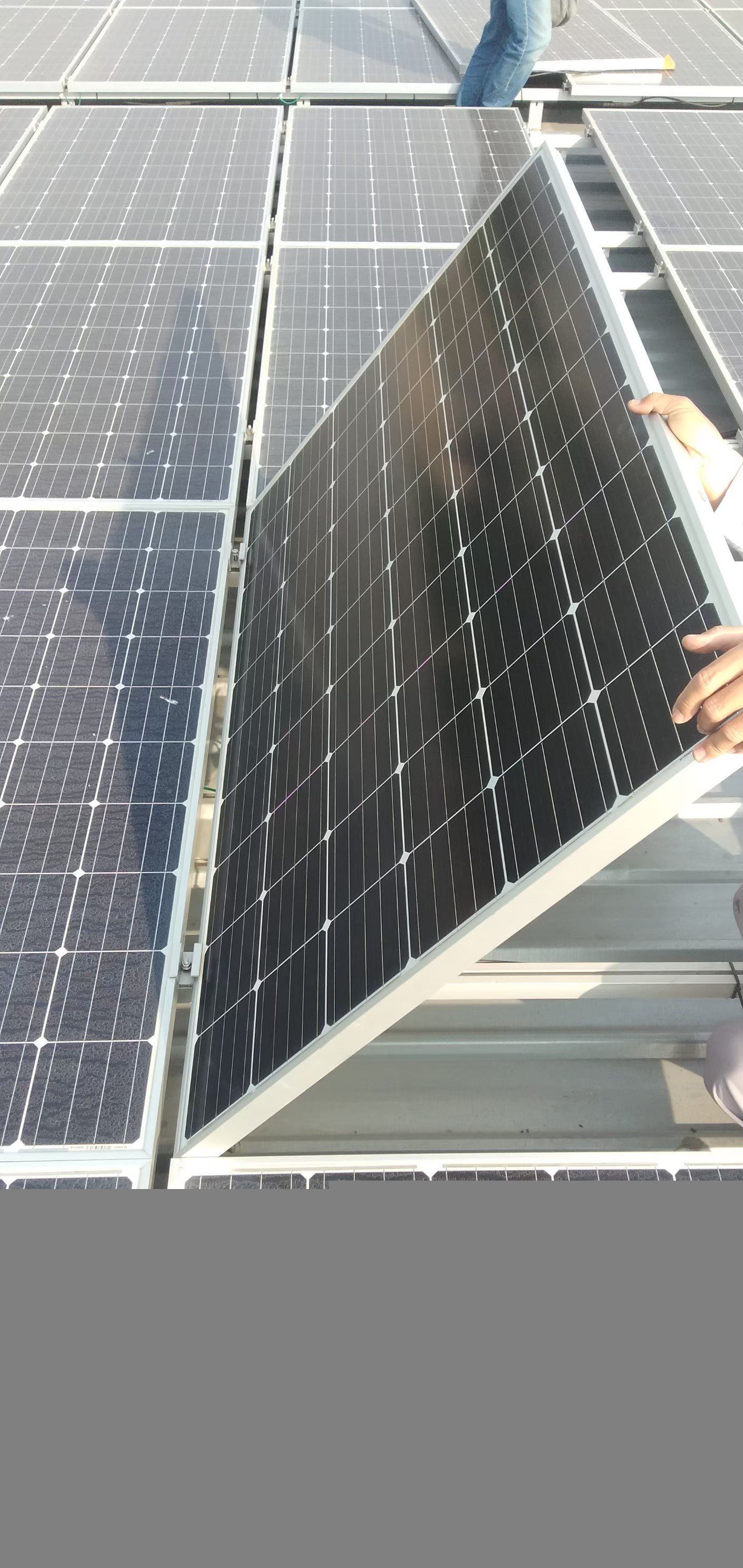 在屋頂陣列上安裝太陽能電池板。一名工作人員正在扶著一塊新的板。
