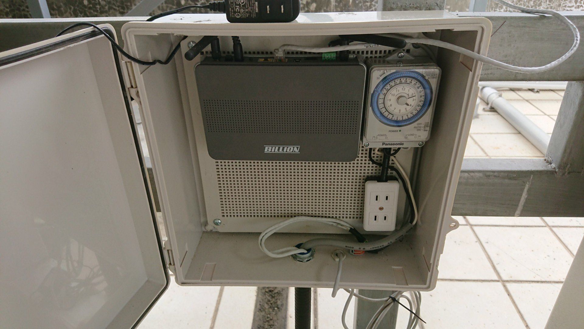 打開一個裝有電子元件的白色盒子，其中包括定時器、電源插座和一個黑色盒子。