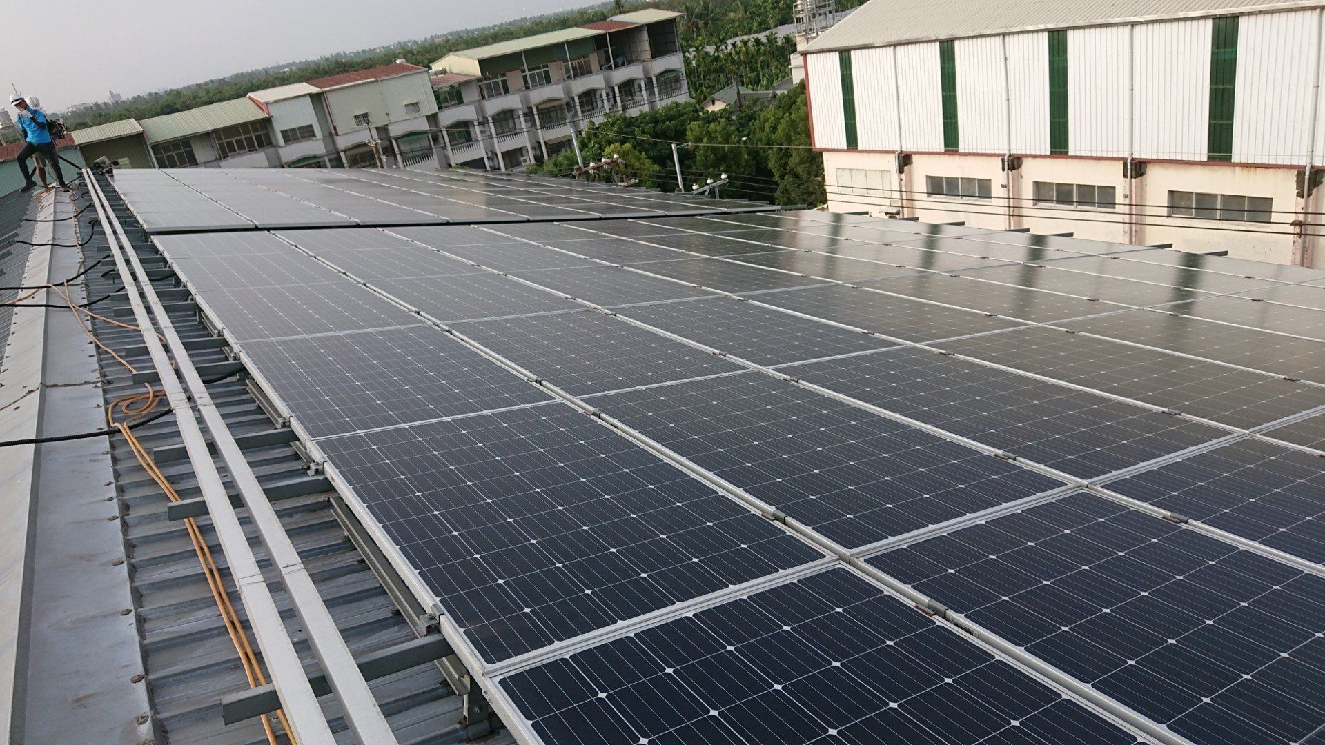 建築物屋頂上的太陽能電池板正在發電。一個人站在屋頂上。