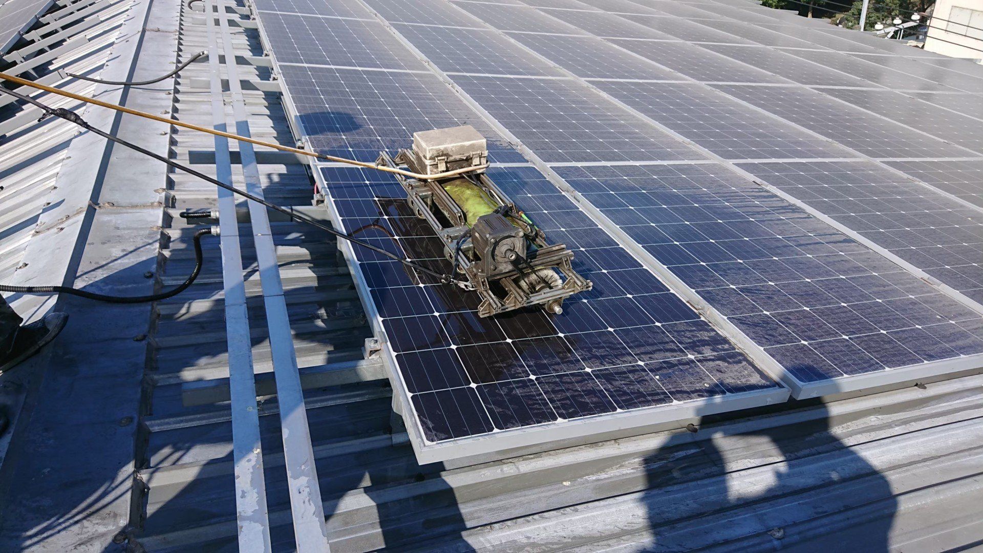 屋頂上的太陽能電池板清潔機器人。在陽光明媚的日子裡，機器人正在清潔深色的電池板。