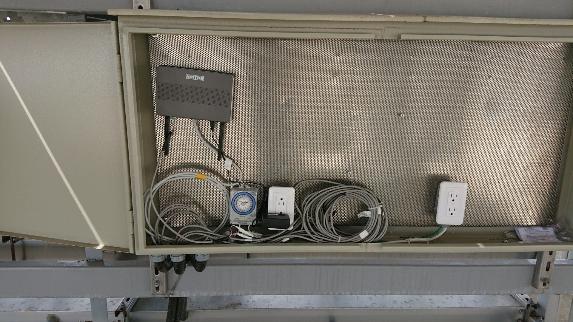 金屬櫃內有電線、電源插座和放在銀色格柵上的黑色小盒子。
