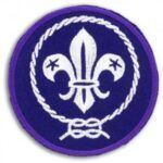 A purple scout badge with a white fleur de lis in a circle.