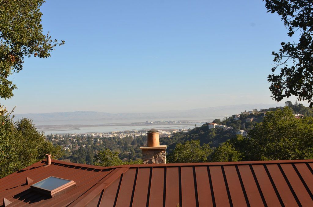 Rooftop view of a hazy valley and distant hills framed by trees under a clear blue sky