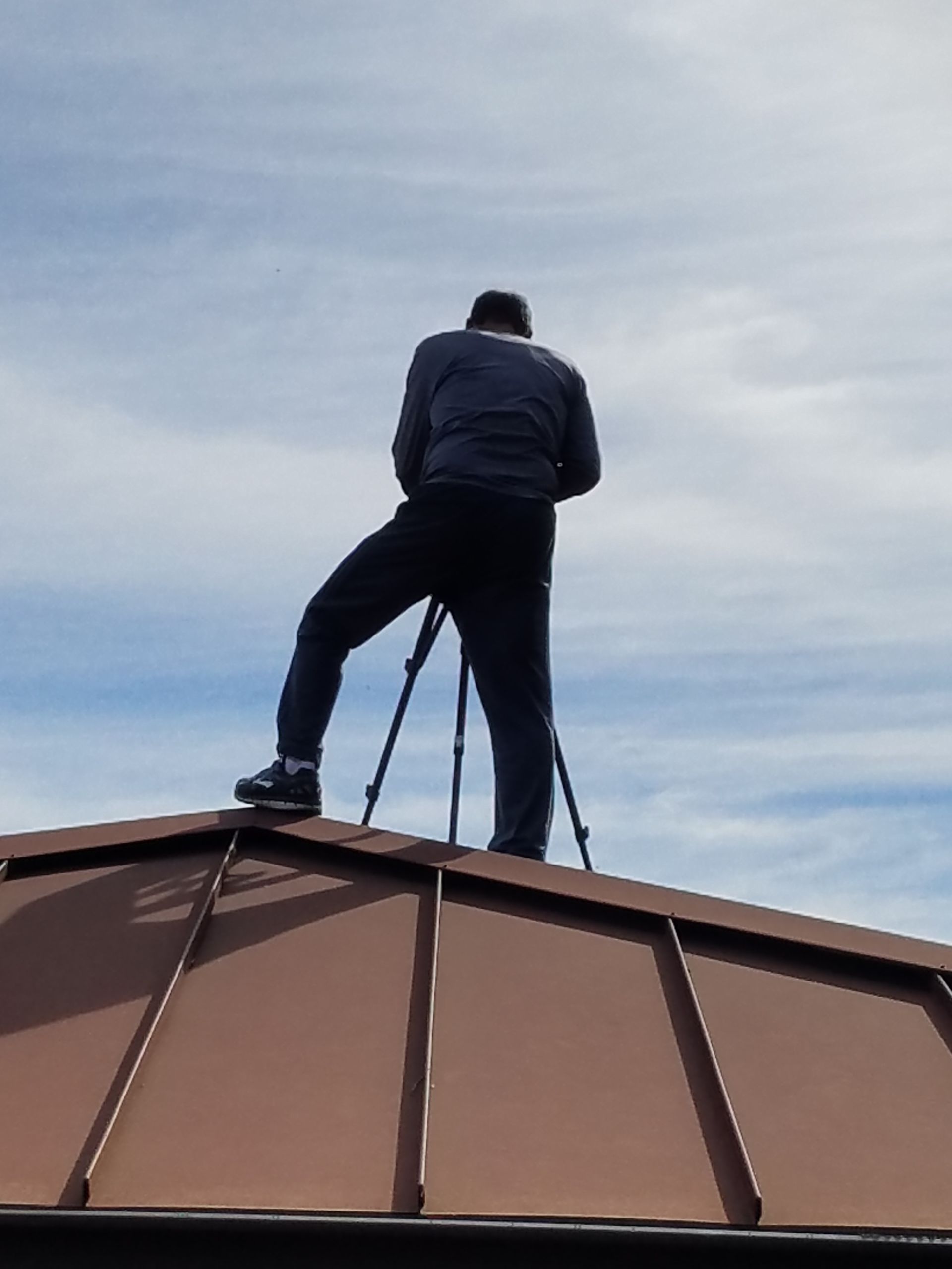 Person standing on a rooftop with a tripod against a cloudy sky