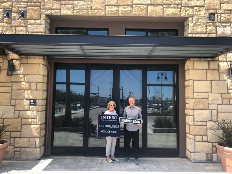 Two people holding signs stand at a glass entrance of a stone building.