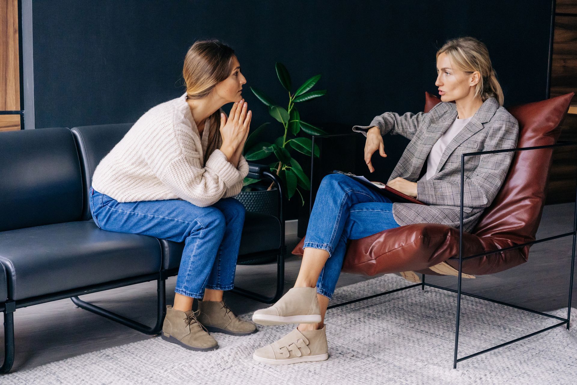 Two women are sitting on a couch and talking to each other.
