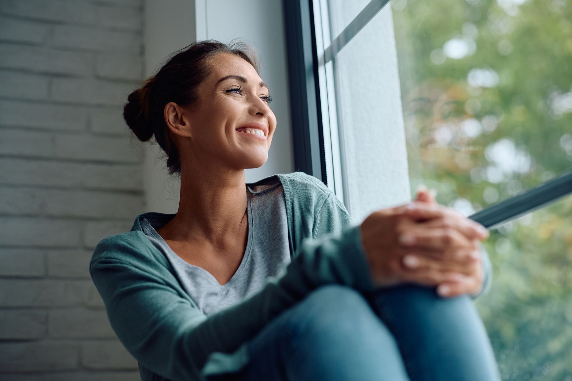 A woman is sitting on a window sill looking out the window.
