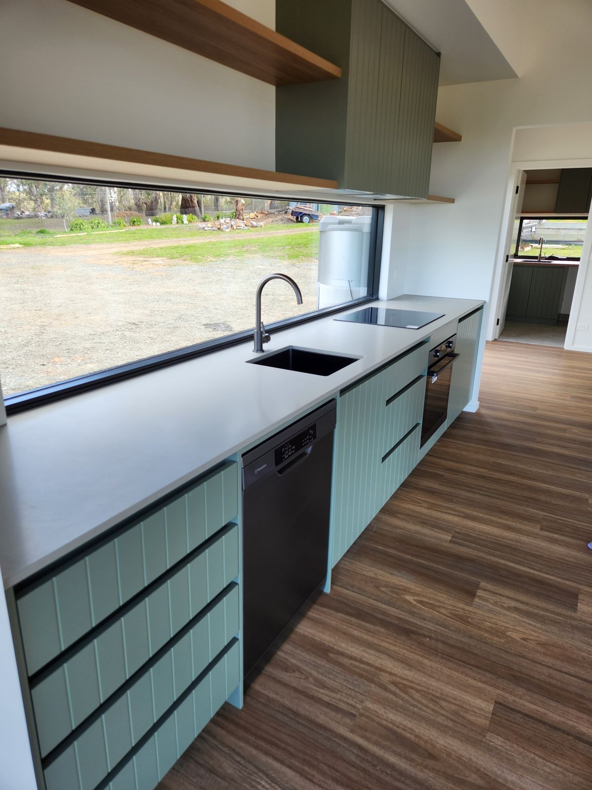 Modern kitchen with light green cabinets, light countertop, dark appliances, and a large window.