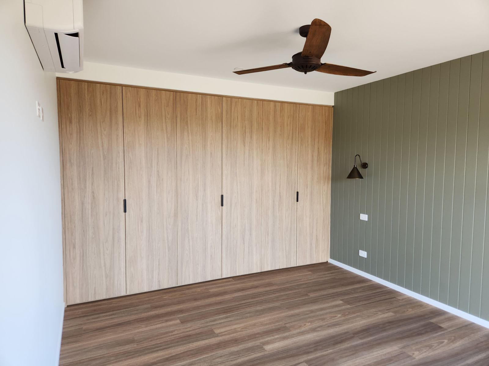 Bedroom with light wood closet doors, olive green accent wall, and wood-look flooring.