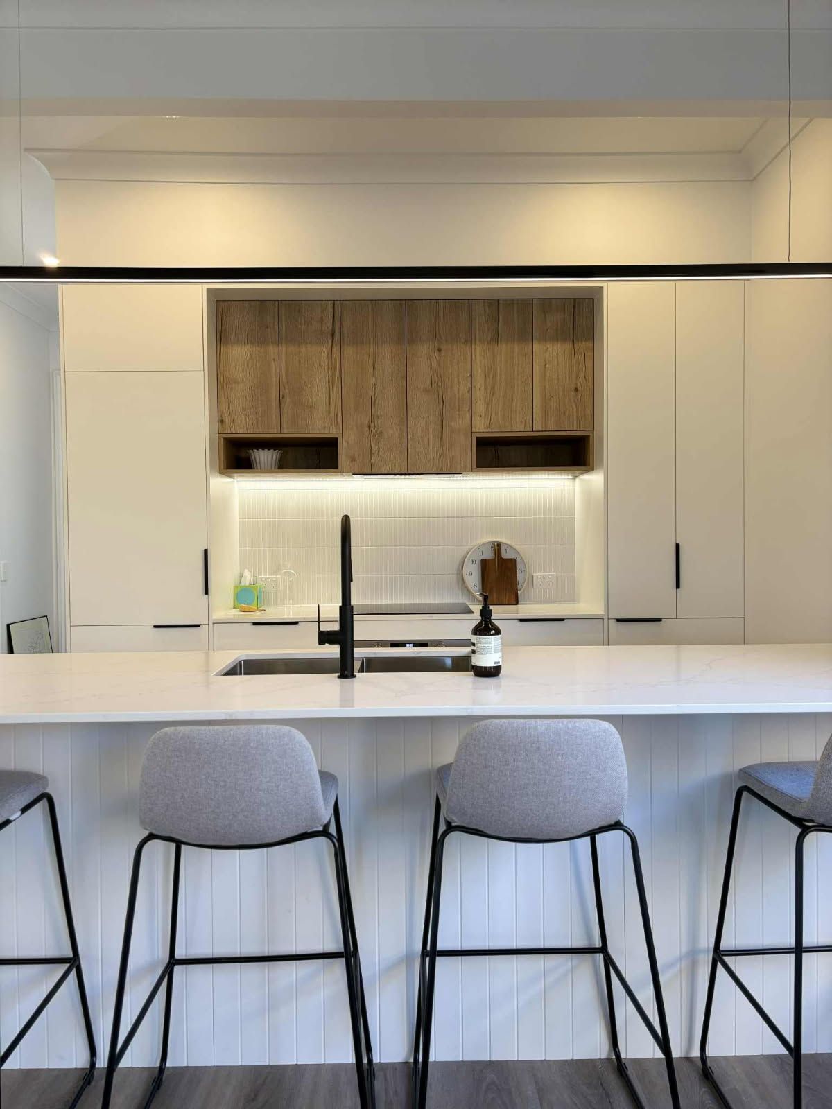Modern kitchen with island, wooden and white cabinets, black faucet, gray bar stools.