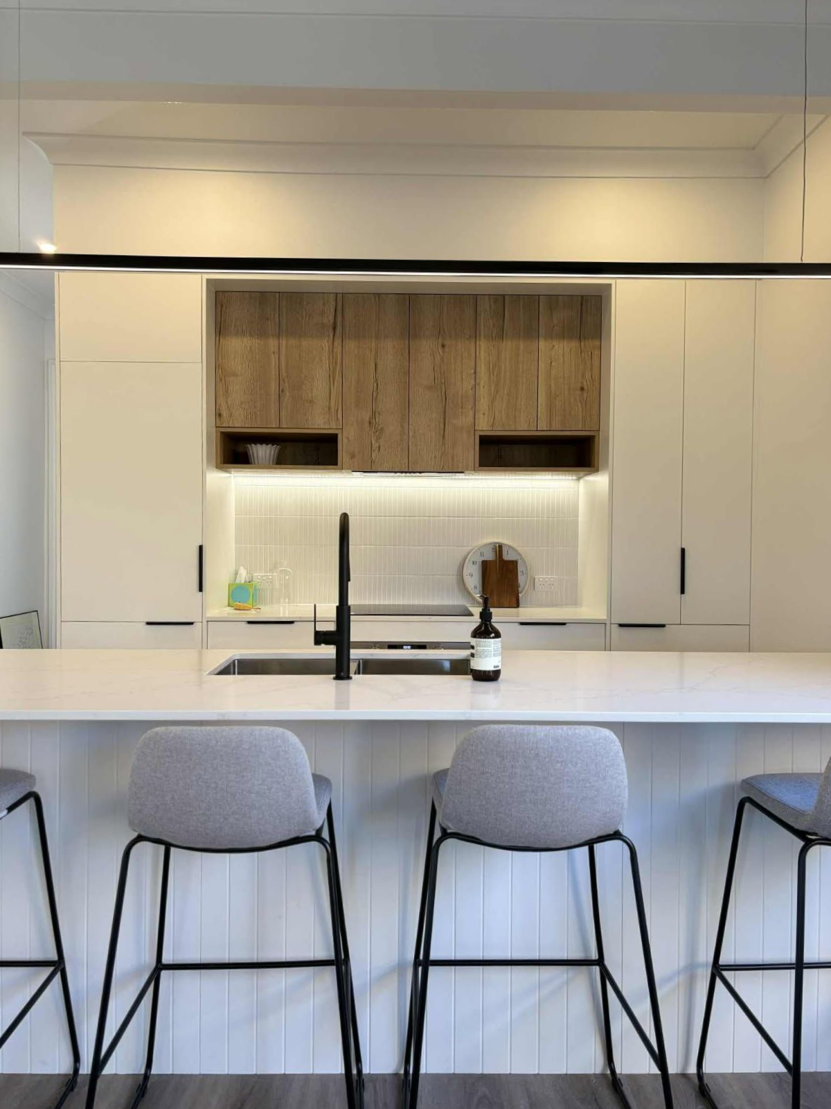 Modern kitchen with white cabinets, wood accents, black faucet, and gray bar stools.