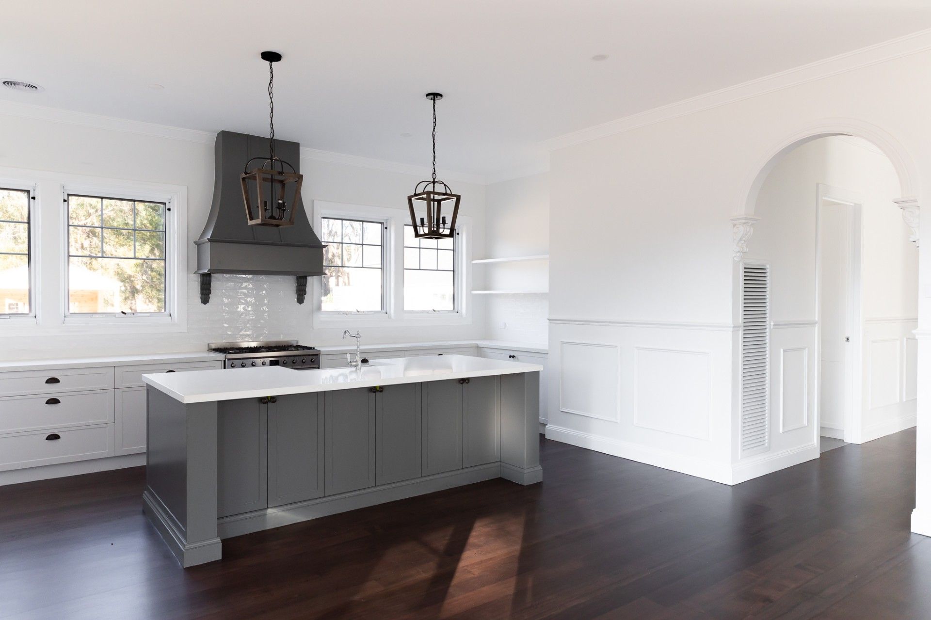 Modern kitchen with gray island, stainless range hood, white cabinets, and dark wood floors.