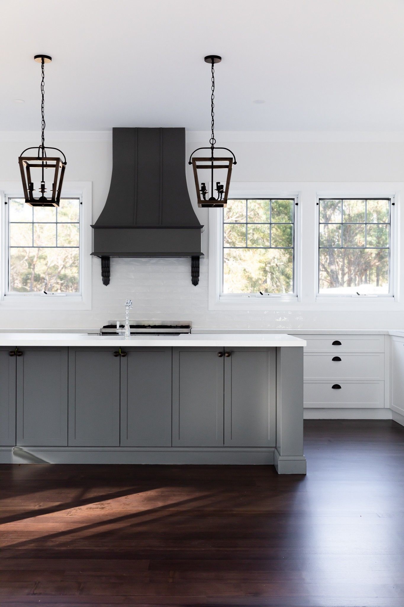 Gray kitchen island with black lantern lights, dark wood floor, white cabinetry.