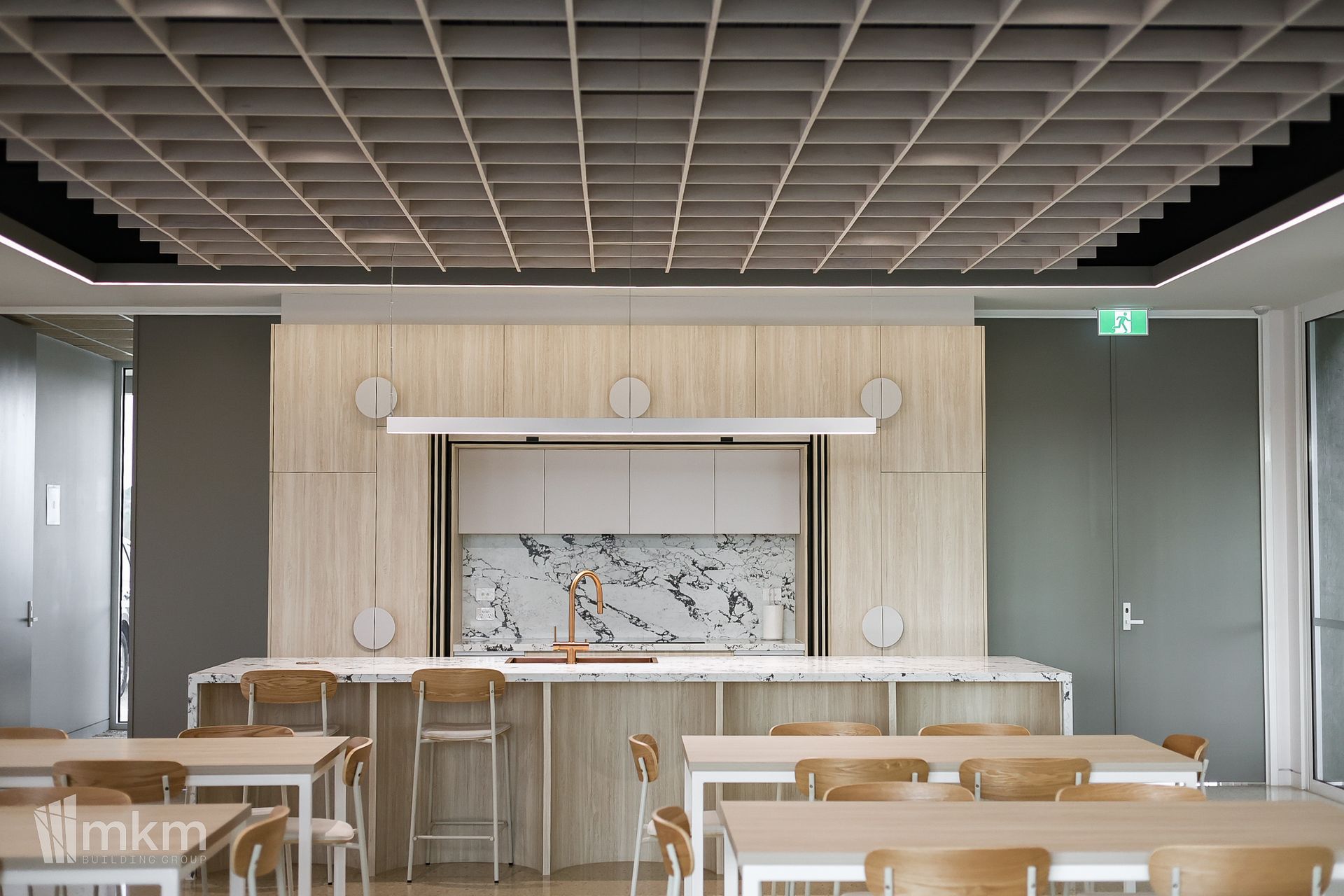 A modern kitchen with a grid ceiling and island with seating. Tables and chairs in the foreground.